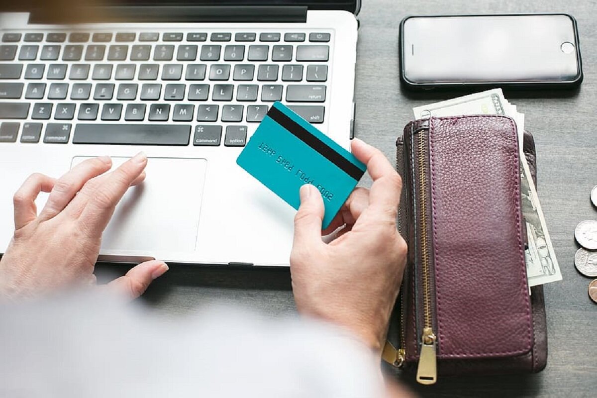 Person am Laptop mit Kreditkarte und Brieftasche mit Geld